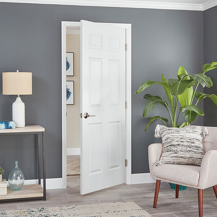 Entrada con puerta blanca lacada, un sillón y una lámpara con planta