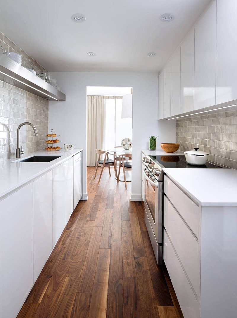 Una cocina moderna alargada en color blanco con suelo de madera